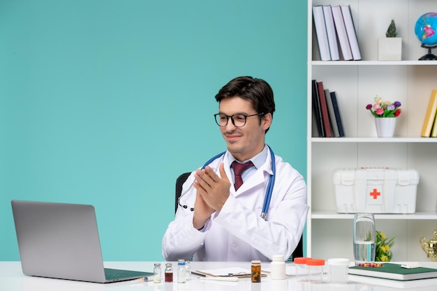 Medical cute handsome doctor in lab coat working remotely on computer clapping hands