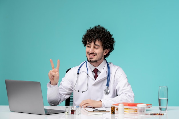 Medical cute handsome doctor working on computer remotely in lab coat showing two sign