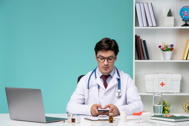 Medical cute smart doctor in lab coat working remotely on computer texting on phone