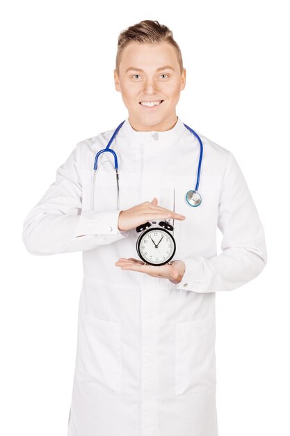 Фото Врач в белом халате со стетоскопом, держащим будильник, тикающий все ближе к 12 часам люди и концепция медицины изображение изолировано на белом фоне студии