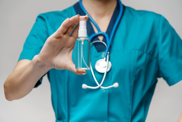 Medical doctor nurse wearing protective mask holding bottle of sanitizing spray or gel