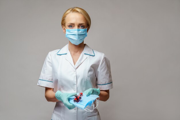 Medical doctor nurse woman wearing latex gloves - holding virus blood test and protective mask