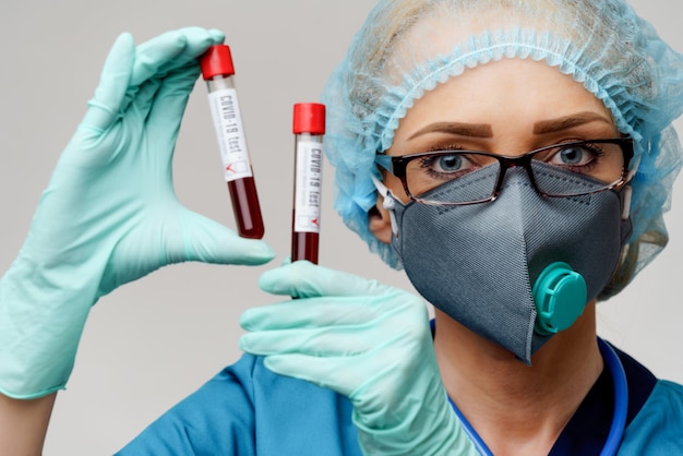 Medical doctor nurse woman wearing protective mask and gloves - holding negative and positive coronavirus COVID-19 blood test