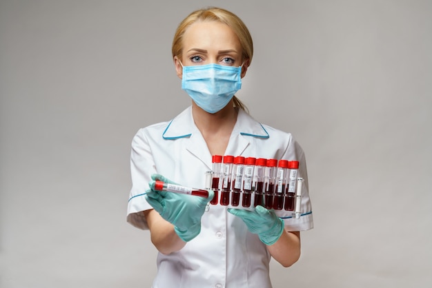 Medical doctor nurse woman wearing protective mask and gloves - holding rack with virus blood tests