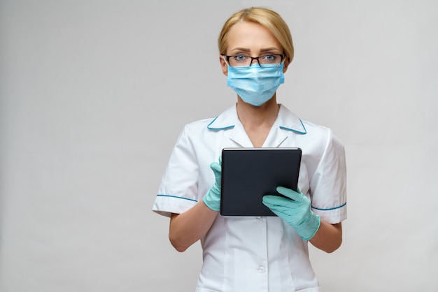 Medical doctor nurse woman wearing protective mask and gloves - holding tablet pc