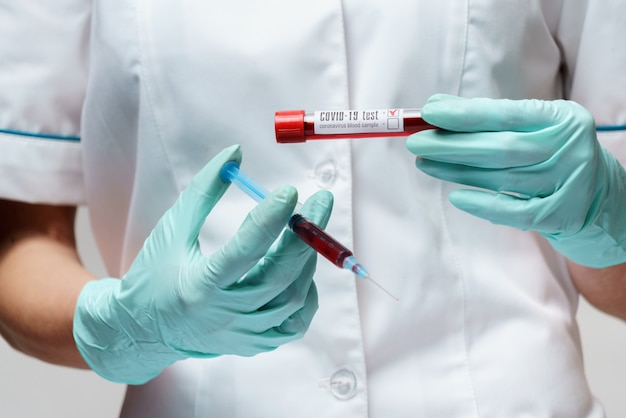 Medical doctor nurse woman wearing protective mask and gloves - holding virus blood test and syringe