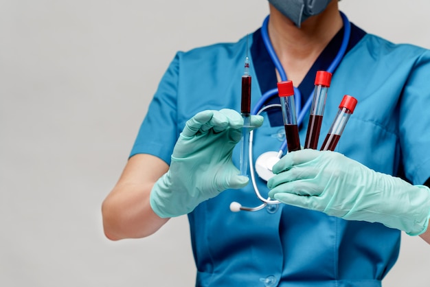 Medical doctor nurse woman wearing protective mask and gloves - holding virus blood test tube and syringe