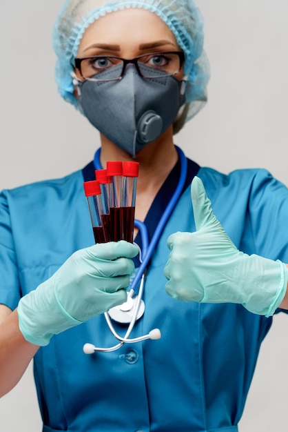 Medical doctor nurse woman wearing protective mask and gloves - holding virus blood test tube