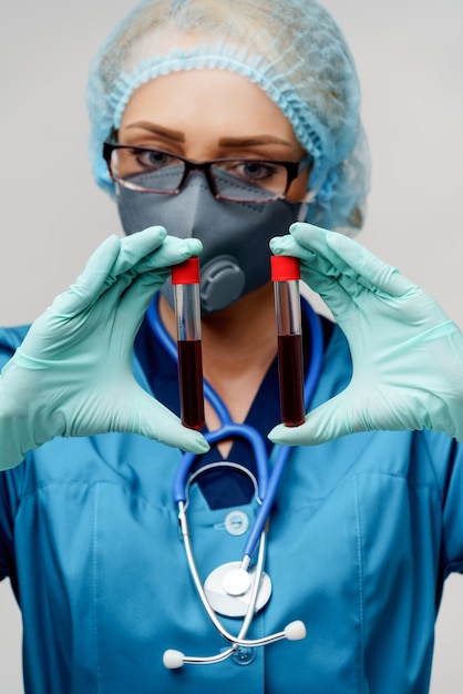 Medical doctor nurse woman wearing protective mask and gloves - holding virus blood test tube
