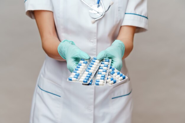 Medical doctor nurse woman wearing protective mask and latex gloves holding blisters of pills