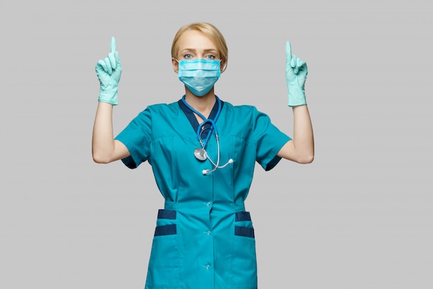 Medical doctor nurse woman wearing protective mask and latex gloves - point up a finger at empty copyspace