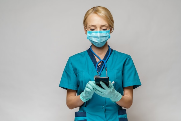 Donna dell'infermiere del medico che indossa i guanti protettivi del lattice e della maschera - facendo uso del telefono cellulare