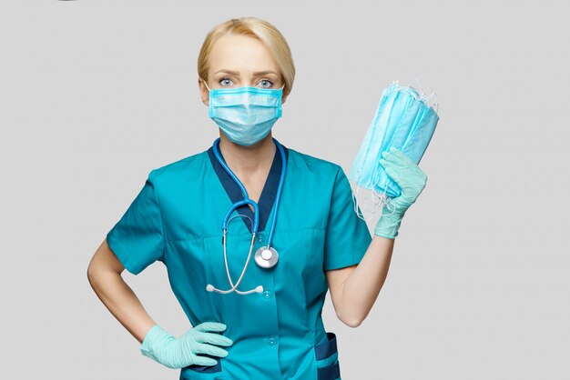 Medical doctor nurse woman with stethoscope over light grey wall - showing protective mask