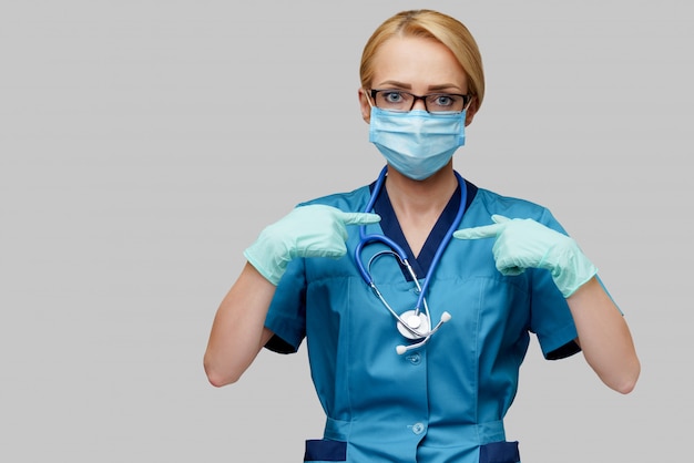 Medical doctor nurse woman with stethoscope wearing protective mask and latex gloves showing at herself