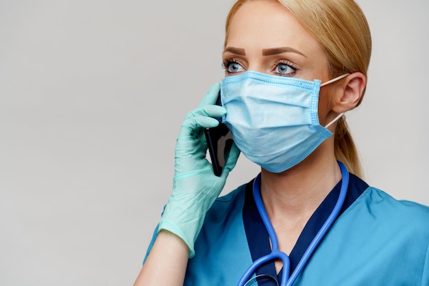 Medical doctor nurse woman with stethoscope wearing protective mask and rubber or latex gloves talking on mobile cell phone