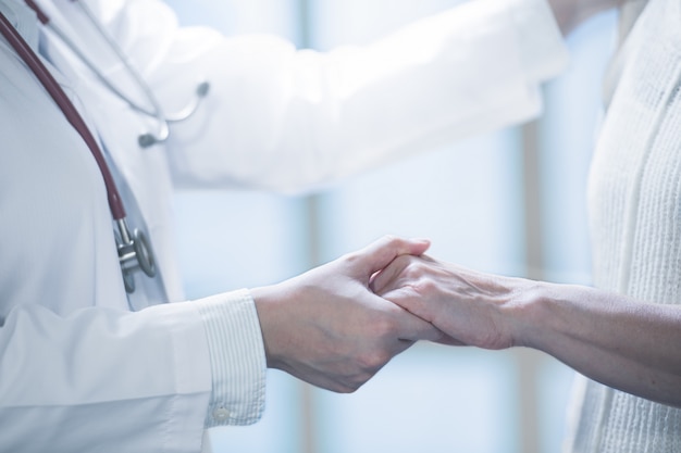 Medical doctor reassuring patient by holding hands in hospital setting