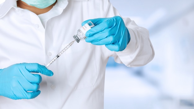 Medical doctor in uniform holding tube with Coronavirus vaccine and syringe.