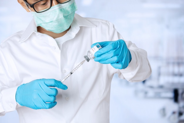 Medical doctor in uniform wearing face mask protective holding tube with Coronavirus vaccine and syringe. Healthcare And Medical concept.