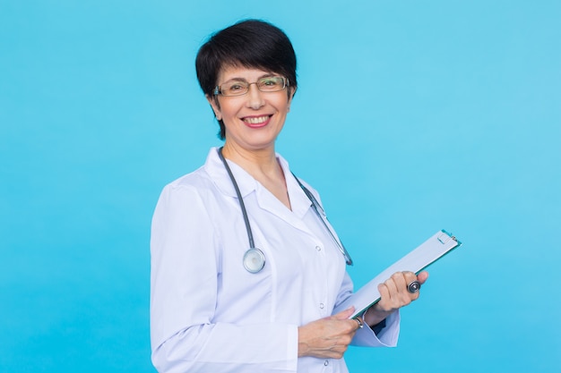 Medical doctor writing prescription over blue background with copyspace