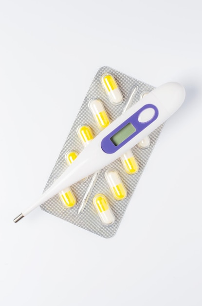 Медицинский электронный термометр и таблетки на белом фоне Концепция диагностики и лечения заболеваний