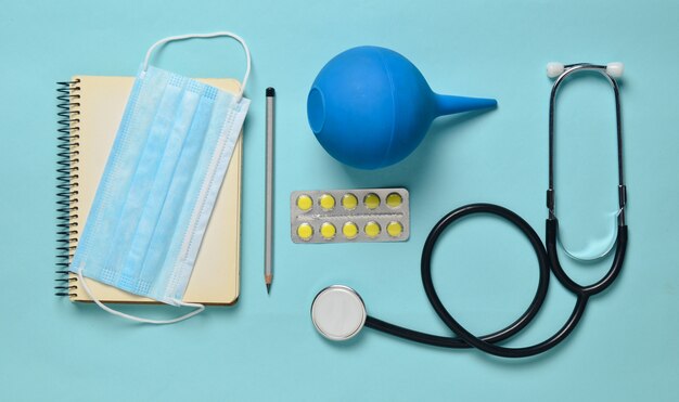 Photo medical equipment on a blue background. enema, blisters pills, notepad, stethoscope, syringe, thermometer. medical concept, top view, flat lay style