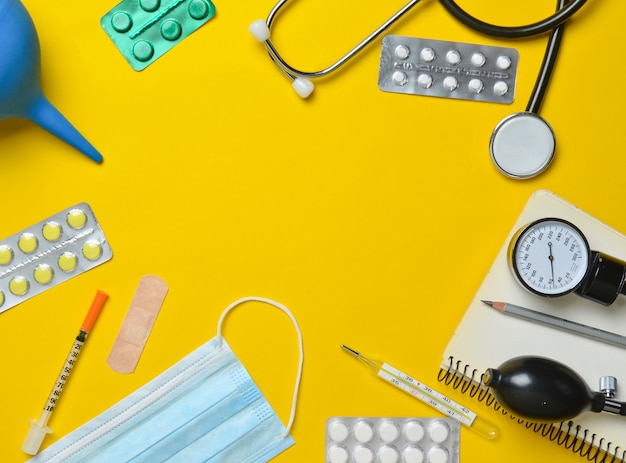 Medical equipment on a yellow background. Enema, blisters pills, notepad, stethoscope, syringe, thermometer, manometer. Medical concept, top view, flat lay style, copy space