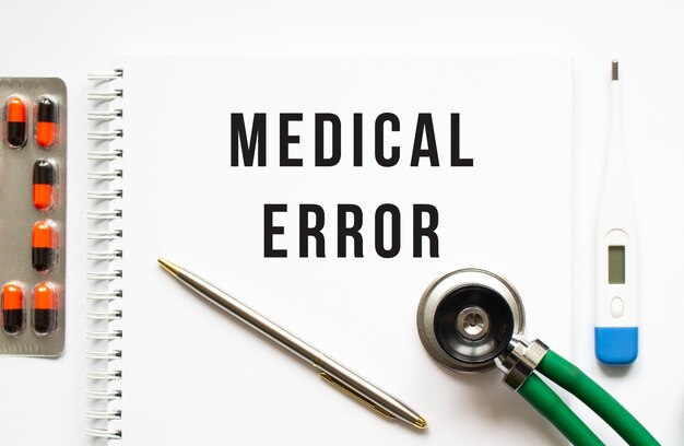 Photo medical error is written in a notebook on a white table next to pills and a stethoscope