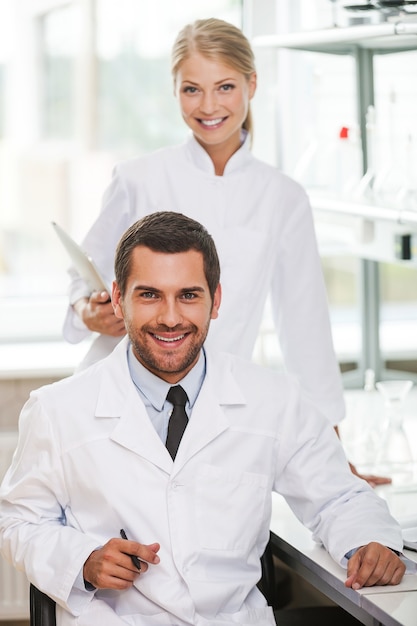 Медицинские специалисты. Два счастливых молодых ученых смотрят в камеру и улыбаются, работая вместе в лаборатории