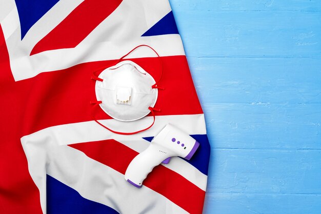 Фото Медицинская маска для лица и бесконтактный термометр на британском флаге, концепция коронавируса