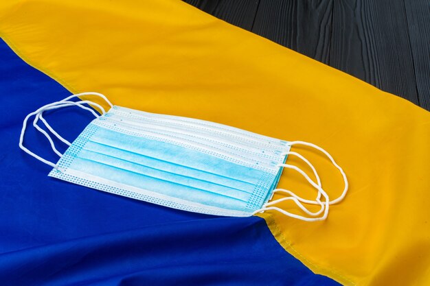 Medical face mask on the flag of Ukraine on wooden board