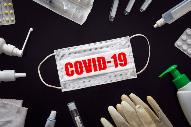 검은 탁자 배경에 COVID-19라는 문구가 있는 의료용 얼굴 마스크와 약. 새로운 코로나바이러스 코로나바이러스 개념. 바이러스와의 싸움. 자가격리를 위한 자가 격리.