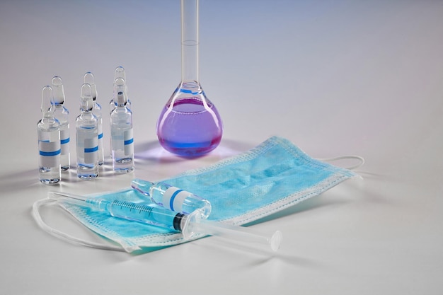 보라색 화학 시약이 있는 의료 플라스크 7개 모형 앰플 주사기와 흰색으로 격리된 마스크
