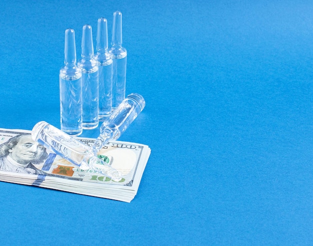 Medical glass ampoules and dollars on a blue background The financing of medicine and the profits of pharmaceutical companies