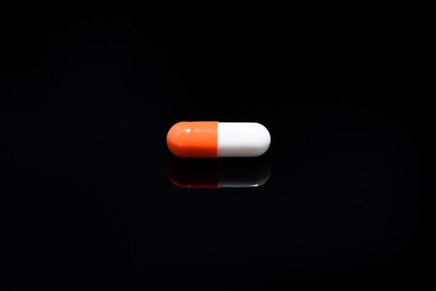 Medical and health care concept: capsules scattered on reflective black background. 