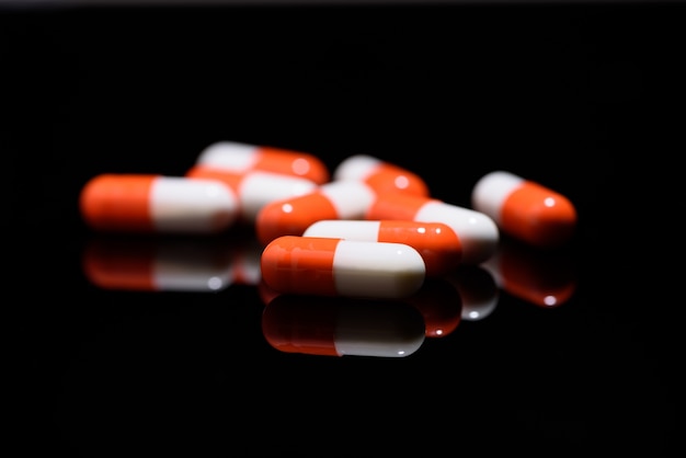 Medical and health care concept: capsules scattered on reflective black background. 
