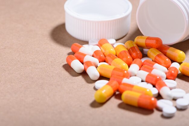 Medical and health care concept: medicine bottle opened,  heaps of capsules scattered on brown background. 