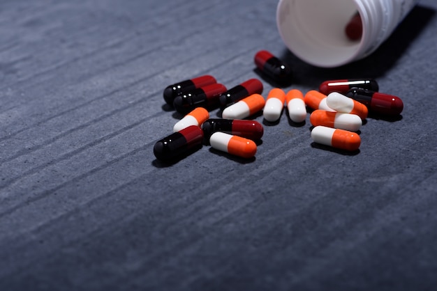medical and health care concept: medicine bottle opened,  heaps of capsules scattered on dark background. 