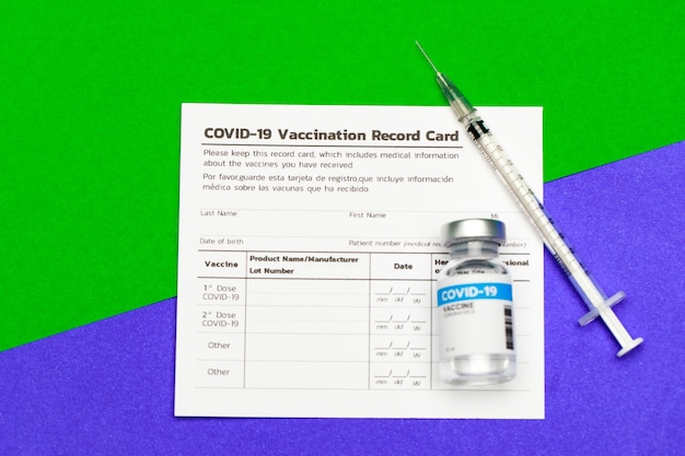 Photo medical injected syringe and sealed glass capsule of covid-19 vaccine on vaccination record card put across borderline of green and purple area looks as immunity safe and infection risk zone.