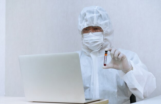 Medical laboratory technician wearing chemical protective Clothing holding COVID-19 positive blood sample tube for test and analysis