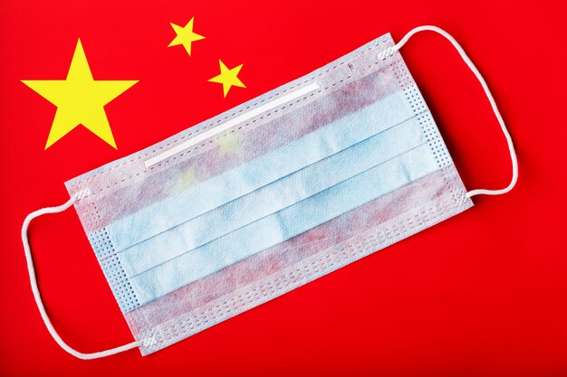 中国の旗の背景に医療マスク。ウイルス用の使い捨てフェイスマスク、コロナウイルス