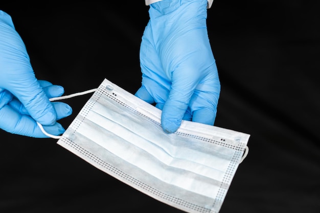 Medical mask and doctor's hands in blue gloves on a black background Protection against coronavirus and other viral infections