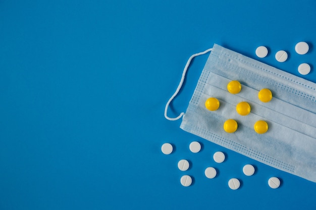 Medical mask on face and white and yellow pills from above