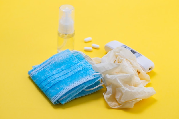 Medical mask, gloves and disinfectant on yellow background