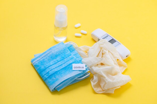 Medical mask, gloves and disinfectant on yellow background