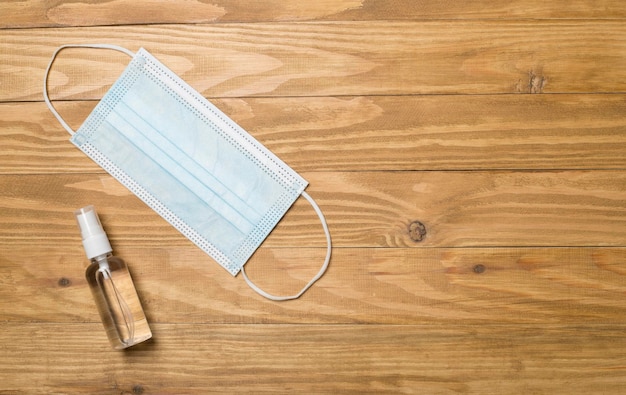 Medical mask and hand sanitizer on wooden background Top view flat lay