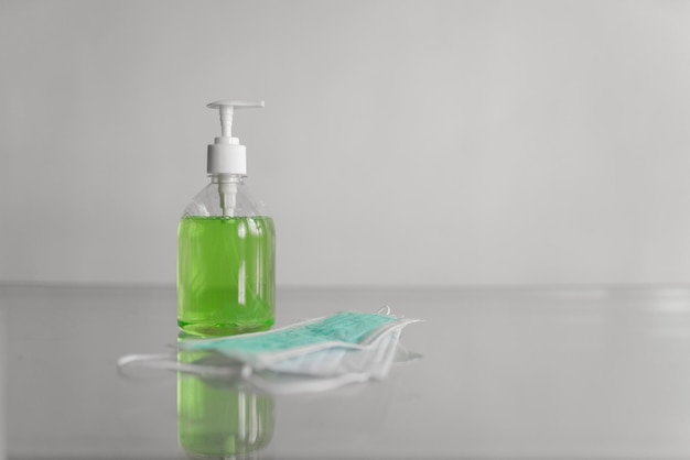 Medical mask lies on the table next to a bottle of liquid soap on a white background