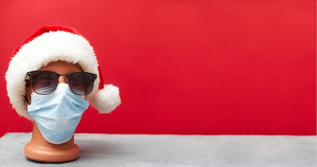 Foto maschera medica su un manichino e un cappello di capodanno natale 2021 su sfondo rosso