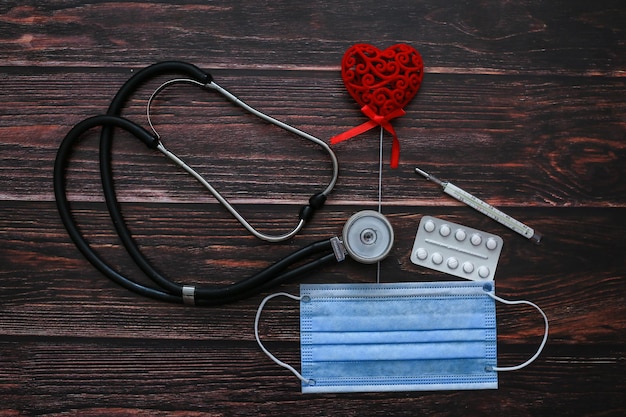 A medical mask a stethoscope a red heart and a red heart on a wooden table