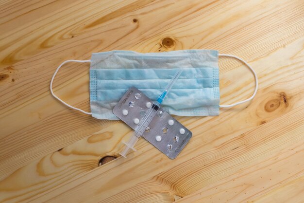 Medical mask, syringe, pills lying on a wooden table