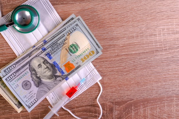 Medical mask, syringe, stethoscope and hundred dollars bills lies on table..